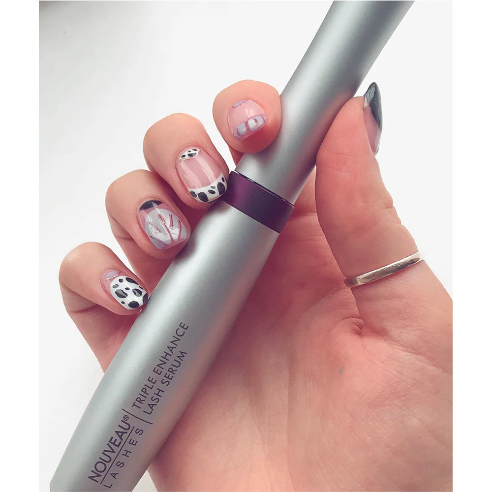 Hand holding Nouveau Lashes triple enhance serum with decorative nails on a white background