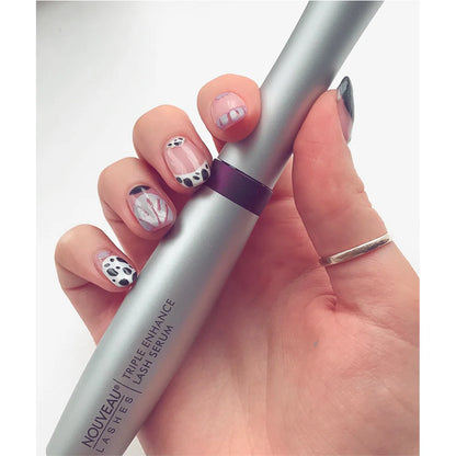 Hand holding Nouveau Lashes triple enhance serum with decorative nails on a white background