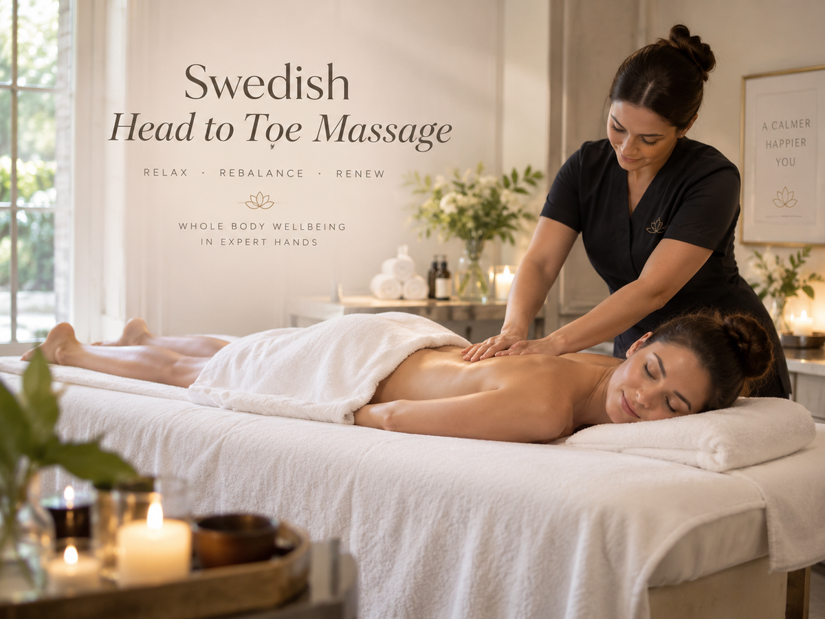A woman receives a Swedish head-to-toe massage on a white treatment table in a bright spa room, with a therapist standing beside her. Text on the wall reads 'Swedish Head to Toe Massage' and 'Whole Body Wellbeing in Expert Hands.