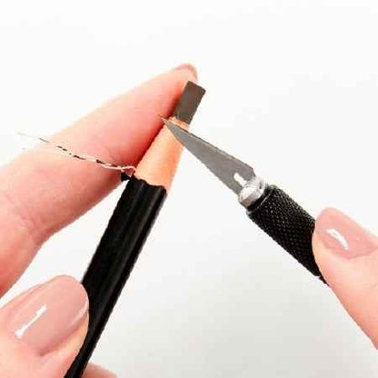 Person using a small knife to sharpen a pencil on a white background